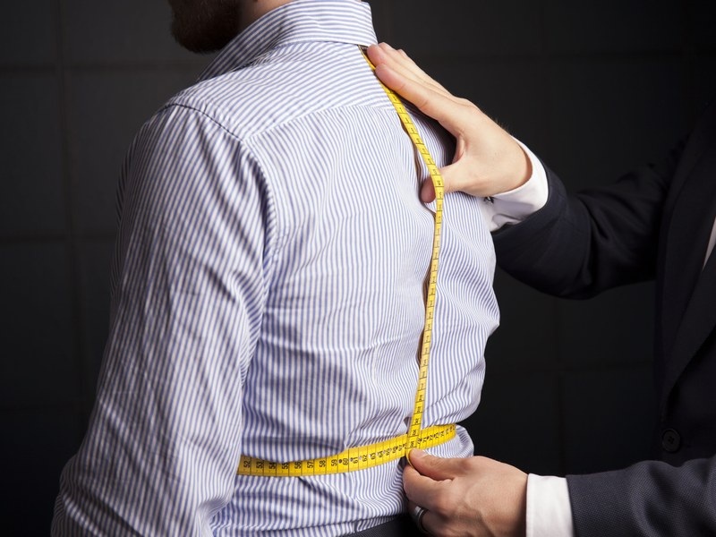 Tailor taking precise anatomical body measurements with measuring tape along customer back and spine